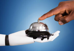 Close-up Of A Person Ringing Service Bell Hold By Robot Against Blue Background